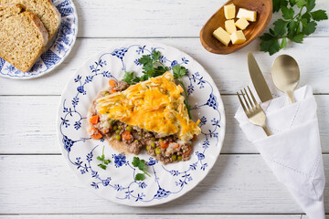 Shepherd's Pie or Cottage Pie on white plate. Savory pie made with beef mince and vegetables topped with mashed potatoes and cheese. View from above, top view