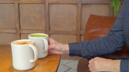 Woman picking up a cup of matcha tea with a cup of coffee