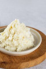 Shea butter in a bowl on a light background, close up. Vertical orientation.