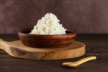 Unrefined raw shea butter in a clay bowl on a table.