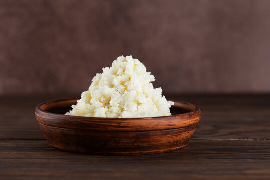Shea butter in a clay bowl on a brown background.