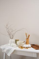 A curated collection of kitchen utensils, vase with dry branches and fresh ingredients: bowl, eggs, milk, sugar, cutboard, napkin is elegantly displayed on a neutral white table.