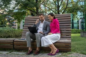 Fototapeta premium Business colleagues using laptop outside of office building.