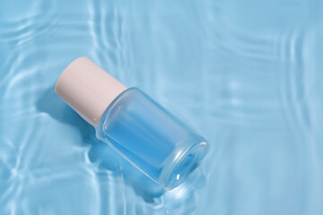 Bottle with moisturizing serum in water on blue background.