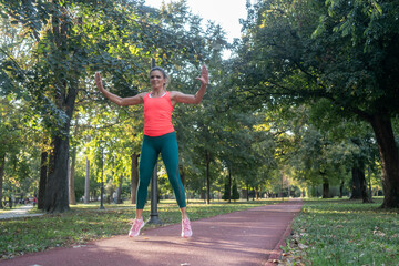 A mature, fit woman and man doing jumping jacks in a city park during summer, enjoying an active...