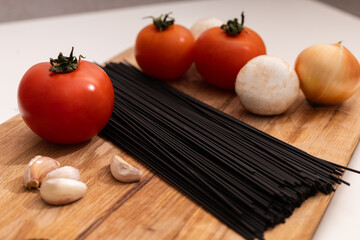 black raw spaghetti and vegetables on a wooden surface