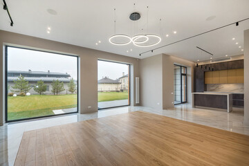A living room in a luxurious private house. Light decor, parquet floor. Panoramic windows with a view of the green landscape.