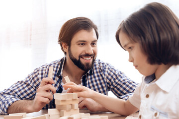 Adult father with small son plays Jenga at home.