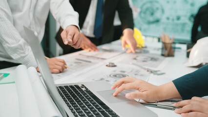 A collaborative team meeting taking place in a modern office where engineers and designers strategize over documents and a laptop, fostering creativity and teamwork. SACTR