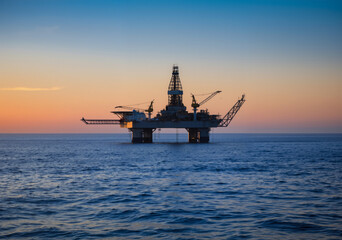 Offshore oil rig stands tall against a vibrant sunset, symbolizing the extraction of fossil fuels from beneath the ocean floor