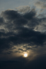 Sun disk among dark rain clouds.