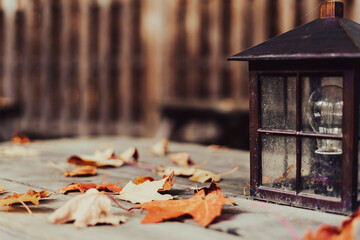 Outdoor lamp on wooden table with fallen autumn leaves