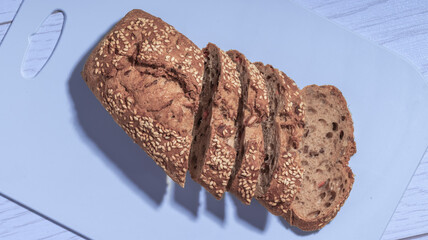 A loaf of whole grain bread with sesame seeds, partially sliced, placed on a light blue cutting board.