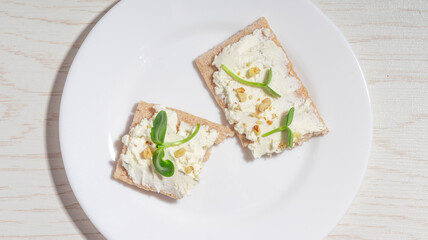 Two crispbread pieces with cream cheese, nuts, and microgreens on a plate, shot from a slightly different angle.