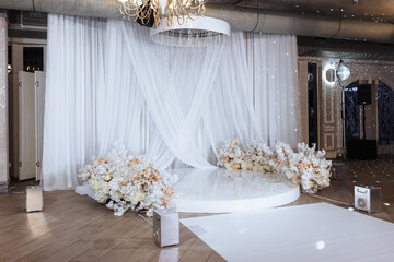 Luxurious wedding arch made of white fabric, roses and podium