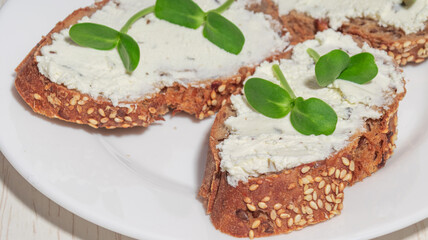 A macro shot of a crunchy slice of seeded bread topped with creamy cheese and fresh green microgreens.