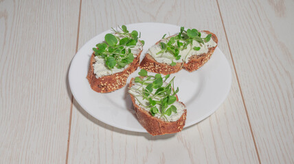 A white plate with three pieces of gourmet bruschetta with cheese and fresh greens, placed on a...