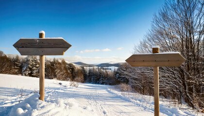Naklejka premium Two rustic wooden signposts covered in snow stand along a snowy trail in a picturesque winter landscape with trees and rolling hills.