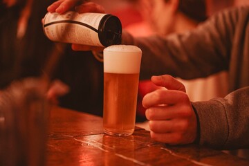 detail of hands of a young adult at the bar of a pub pouring the contents of a can of lager into a glass