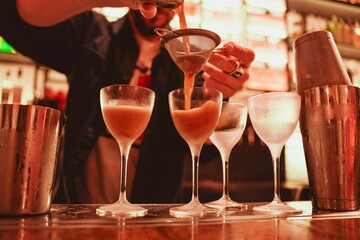 cocktail preparation detail at the bar counter. The bartender prepares three alcoholic drinks by pouring the contents into the glasses with the strainer during an evening party