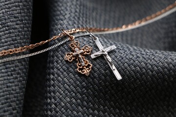 Gold cross pendant and silver cross pendant on textured grey background