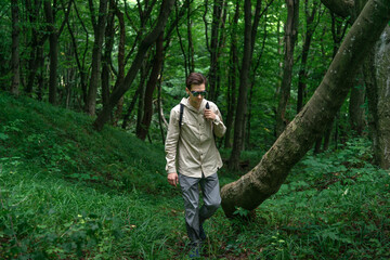 Adventurous man hiking through a forested mountain area, surrounded by lush green trees and dappled sunlight.