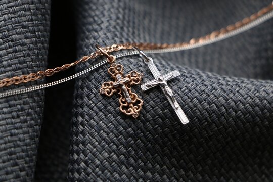 Gold cross pendant and silver cross pendant on textured grey background