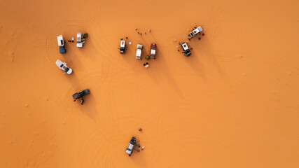 Aerial view of a group of 4x4 campers setting up camp on the desert sand, somewhere in the Admer erg, in the heart of the Algerian Sahara desert