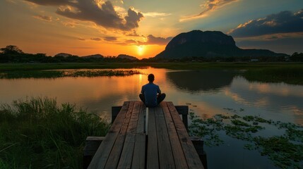 Fototapeta premium Lonely man sitting at wooden bridge with beautiful romantic golden sunset at pond. Fantastic vivid twilight at Sam Roi Yod National Park, Prachuap Khirikhan, Thailand.