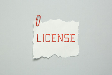 Piece of paper with word License and paperclip on white background, top view