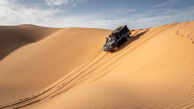 A 4x4 camper equipped with a roof tent crosses a sand dune of the Admer erg in the heart of the Algerian Sahara desert