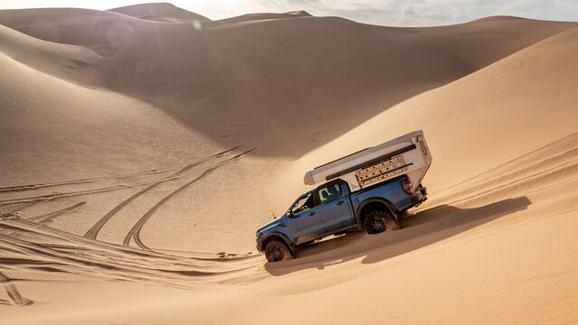 A 4x4 camper  crosses a sand dune of the Admer erg in the heart of the Algerian Sahara desert
