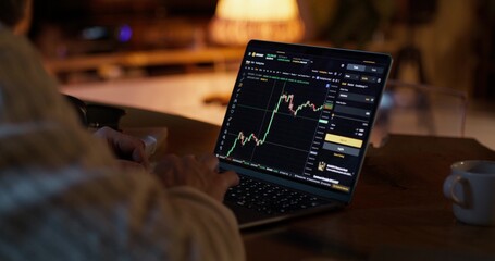 A man participates in trading on the stock exchange, he uses a laptop while sitting at a desk at...