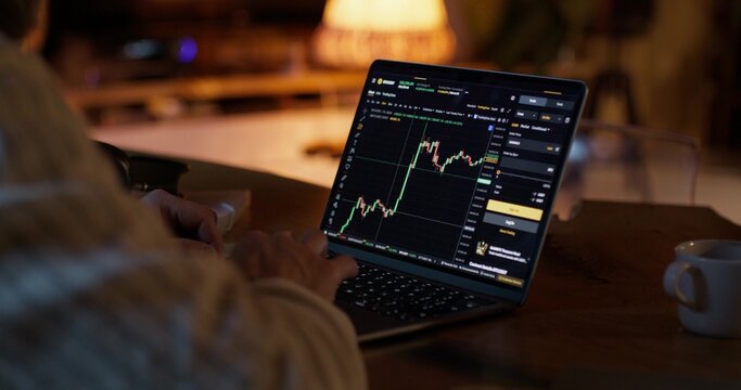 A man participates in trading on the stock exchange, he uses a laptop while sitting at a desk at home. Close-up of his hands, unrecognizable person