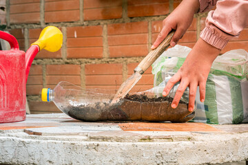 latin girl's hands putting compost and soil for plants in a pot made of a plastic bottle -...