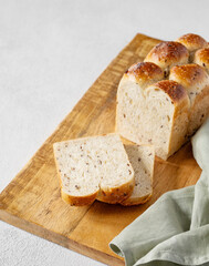 Freshly baked whole grain bread with slices on a wooden board with a napkin on a light background.
