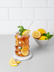 Iced tea with lemon, ice and mint in a glass on the kitchen countertop with citrus fruits