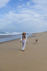 Beautiful young woman walking by the ocean with her dog