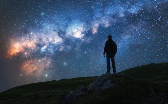 Glowing Milky Way and man on mountain peak at starry night. Silhouette of a guy on the hill, sky with bright stars. Galaxy. Space landscape with milky way. Nightscape. Travel background. Concept
