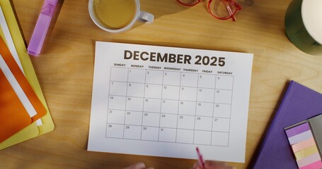 A woman circles a date on a calendar sitting at her desk. Close-up of her hands, unrecognizable...