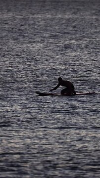 Silhouette of surfer paddling in ocean at sunset, Hawaii
