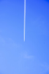 A high-flying jet moves almost vertically, leaving a straight, thin contrail against a deep blue sky