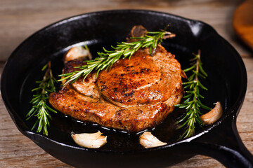 Pork cutlet on the bone in a piece of butter with garlic and rosemary in a frying pan 