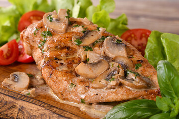 Chicken breast with mushroom sauce and vegetables on a wooden plate