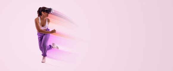 Joyful African American woman enjoying virtual reality experience in modern vr headset, fit young lady enjoying 3D fitness class over pink neon light background, copy space