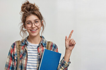 Cheerful young woman with curly updo, glasses, plaid overshirt, and striped shirt, holding a blue notebook and pointing upward with excitement against a white background.
