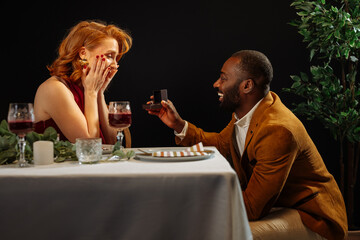 Man proposing marriage to surprised woman during romantic dinner