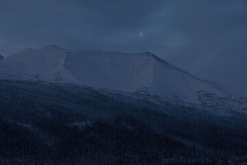 Fototapeta premium Moon over snowy mountain on winter day near Tok, Alaska