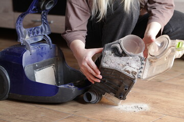 Woman holding household vacuum cleaner container clogged up with dust after an extensive cleaning....