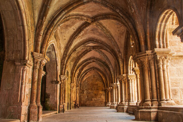 Fototapeta premium Ancient monastery cloister in Porto, Portugal, featuring arched stone corridors and intricate columns bathed in warm sunlight. Stunning medieval architecture and historical atmosphere. 